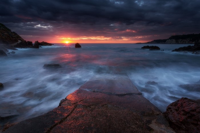 Sunset over the ocean with waves crashing on rocks