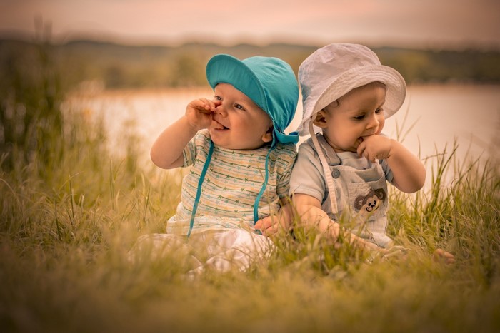 Two babies sitting in grass by a lake