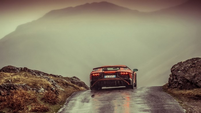 Orange Lamborghini Aventador driving on a wet mountain road