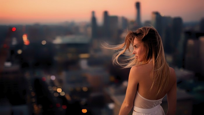 Woman with windblown hair overlooking city at dusk