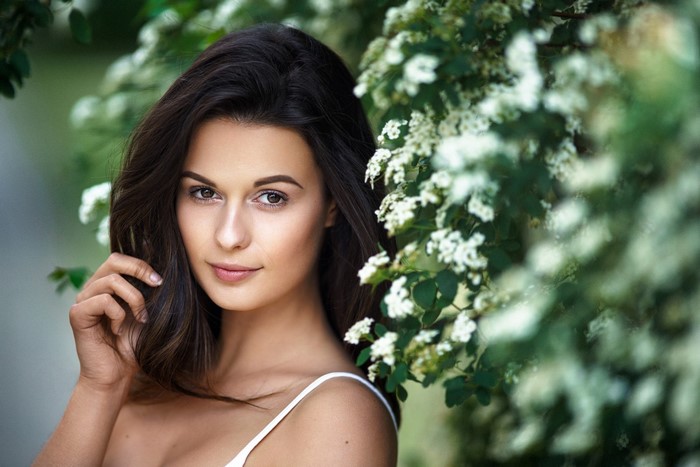 Woman with long dark hair posing near white flowers