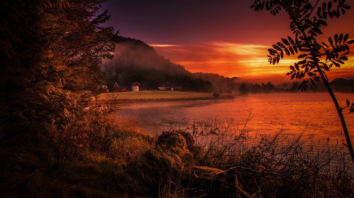Farm buildings by a misty lake at sunset
