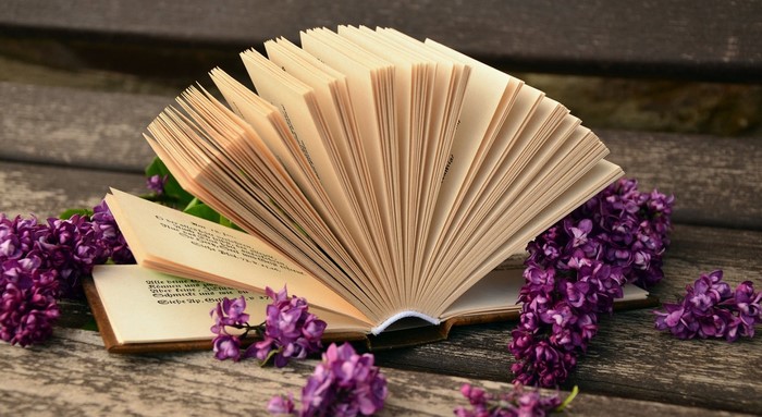 Open book with purple flowers on wooden surface