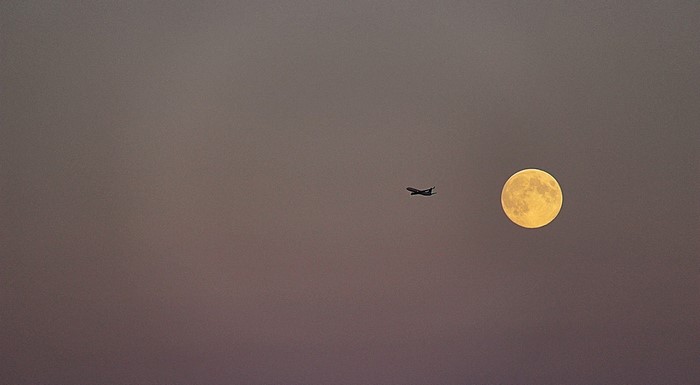 Airplane flying past a full moon in the sky