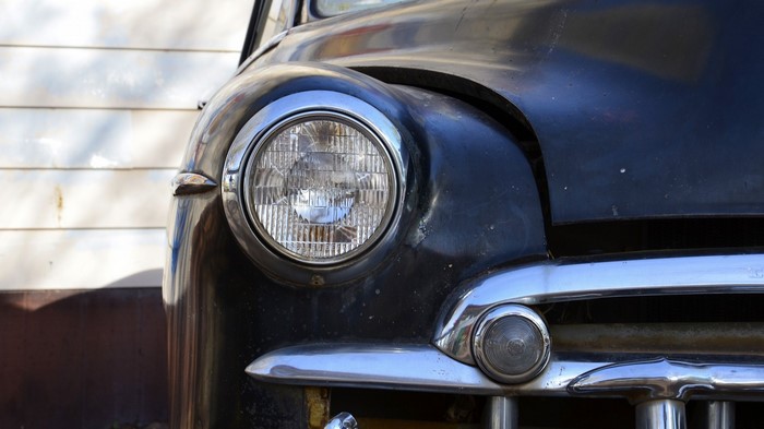 Close-up of a vintage black car headlight and bumper