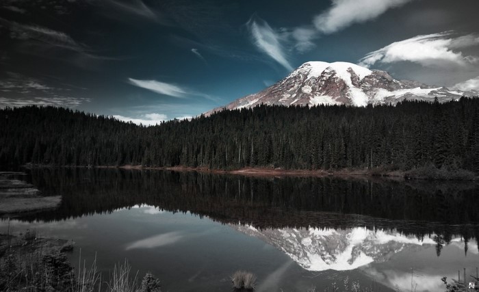 Snow-capped mountain reflected in a dark lake with pine forest