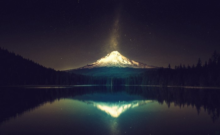 Snow-capped mountain reflected in a lake under a starry night sky