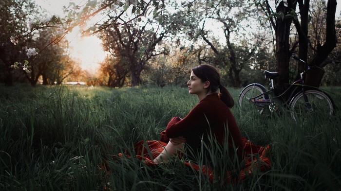 Woman sitting in grass with bicycle in orchard