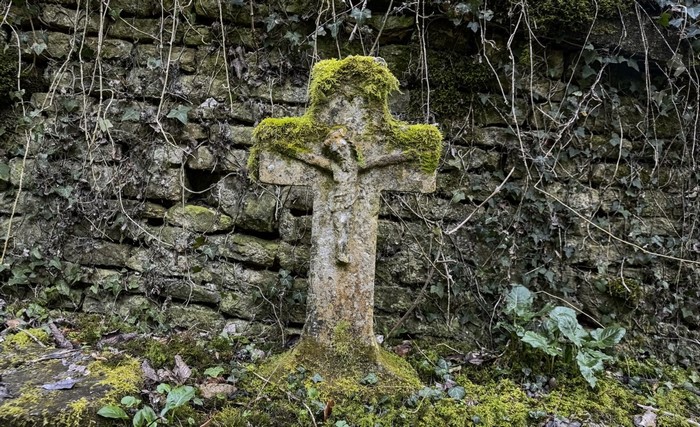 Moss-covered stone crucifix in front of a stone wall