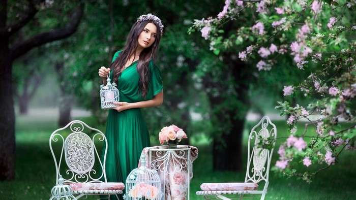 Woman in green dress holding a birdcage in a garden