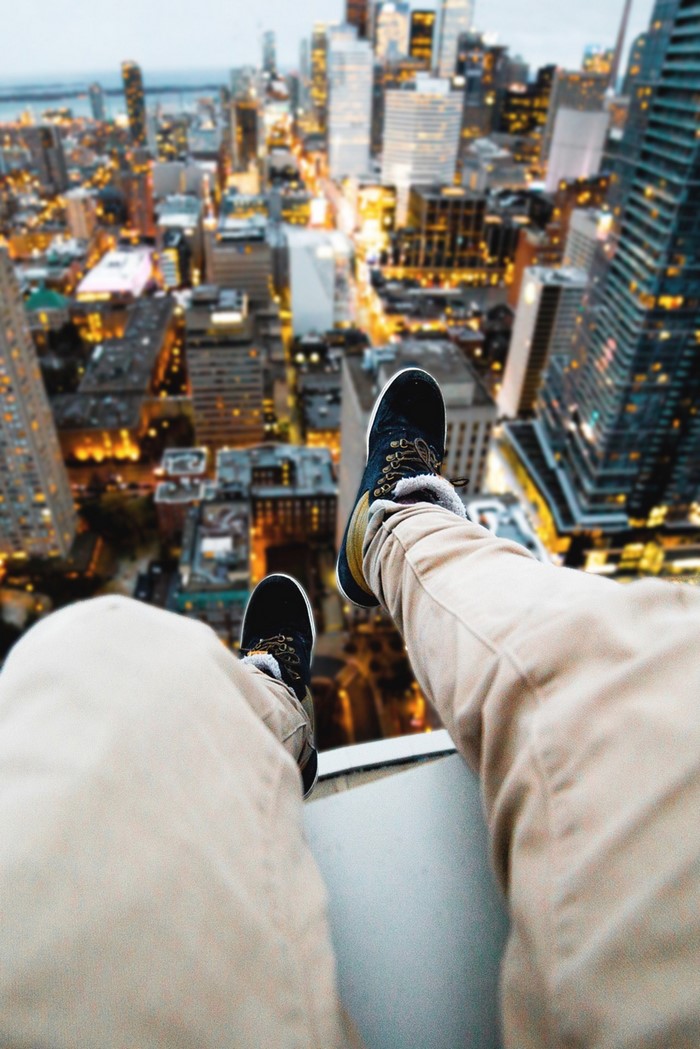 Person sitting on edge of building overlooking city at night