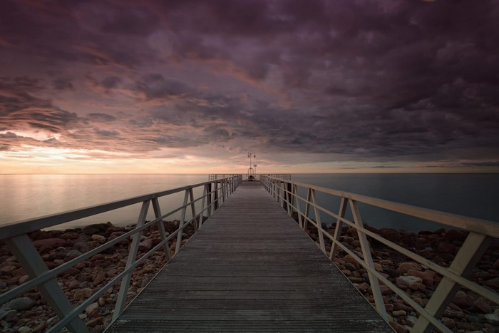 Wooden pier over the sea at sunset with dramatic clouds