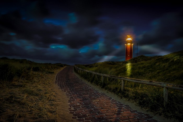 Lighthouse on a dune at night with a brick path