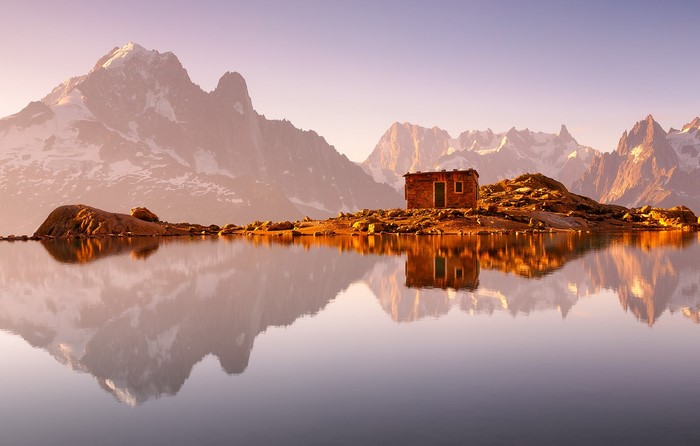 Small house on island with mountain reflection at dawn