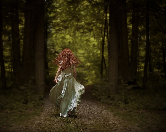 Redhead woman in a dress running on a forest path