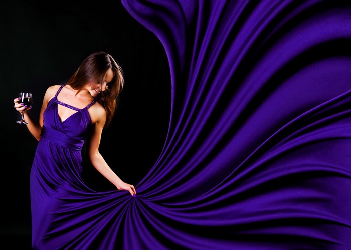 Woman in purple dress holding wine glass with purple fabric