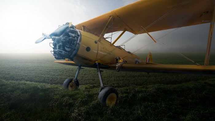 Yellow biplane aircraft in a foggy field