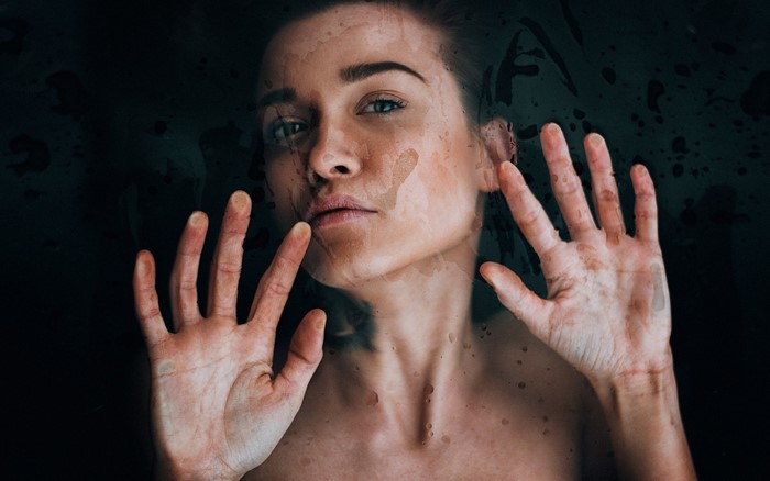 Woman's face behind wet glass with hands