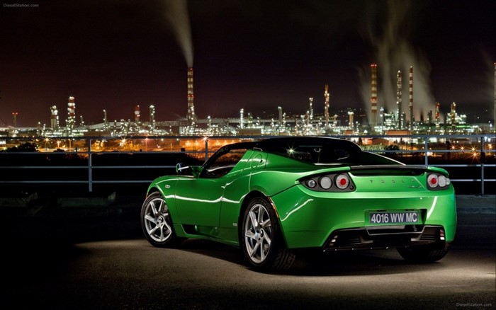 Green Tesla Roadster parked at night with industrial background