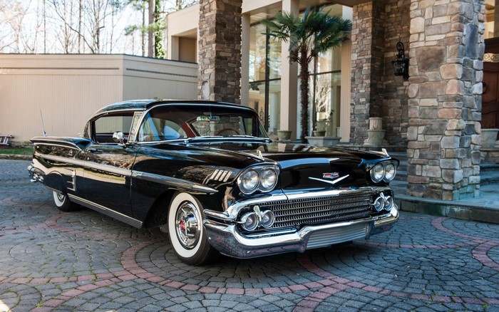 Black 1958 Chevrolet Bel Air parked in front of a stone mansion