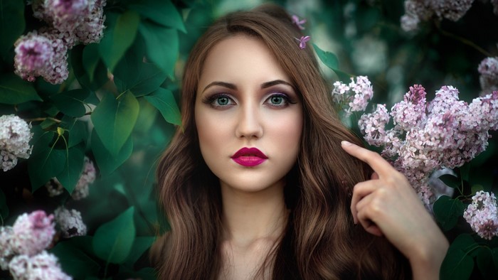 Woman with pink lips and green eyes among lilac flowers