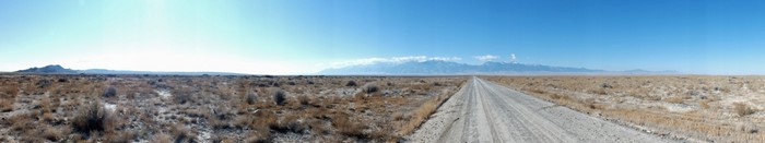 Dirt road through a dry, grassy plain towards distant mountains