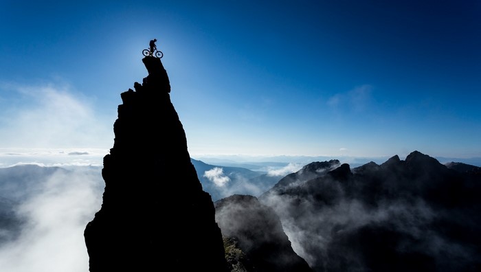 Mountain biker silhouetted on a rocky summit against a bright blue sky