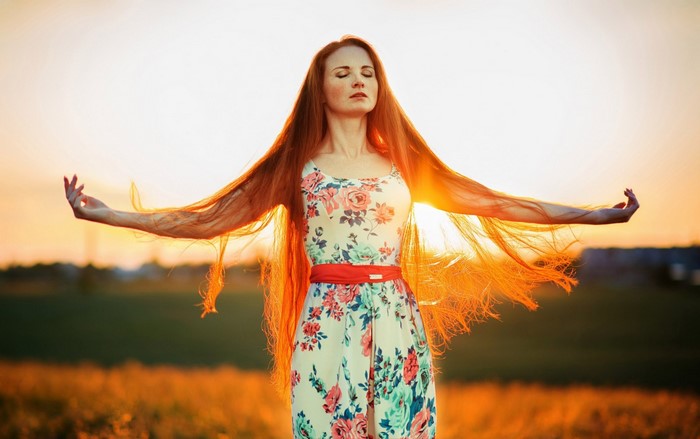 Woman with long red hair in a floral dress at sunset