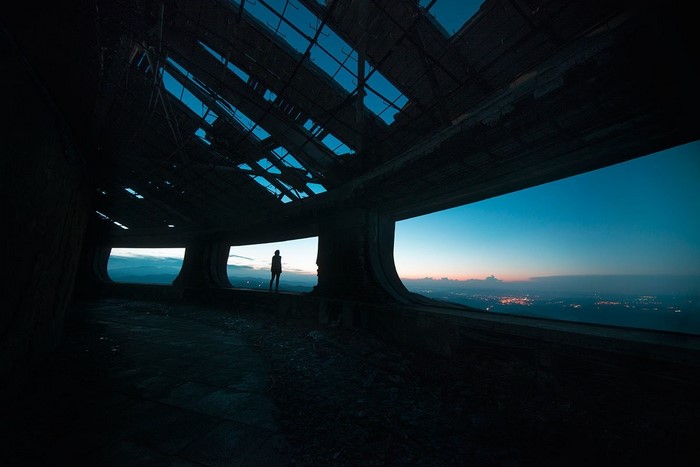 Silhouette of a person in a ruined building overlooking a city at dusk