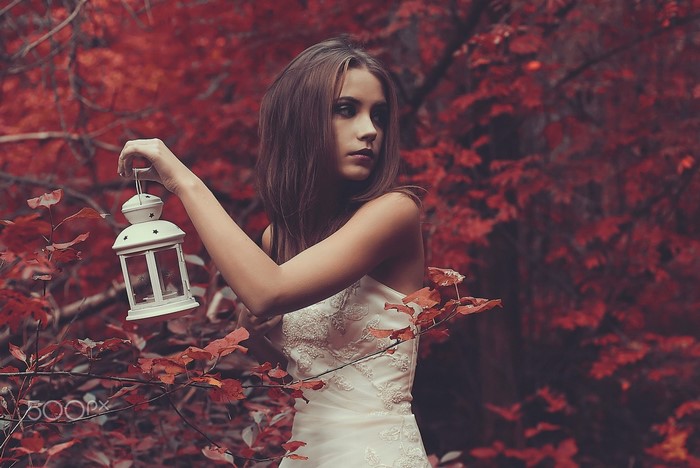 Woman in white dress holding lantern in red forest