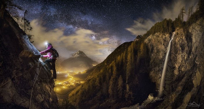 Woman rock climbing at night under the stars with a waterfall