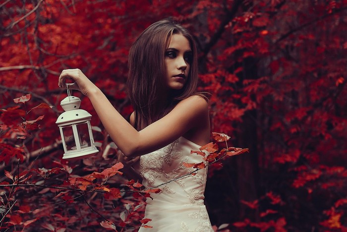 Woman in white dress holding lantern in red forest