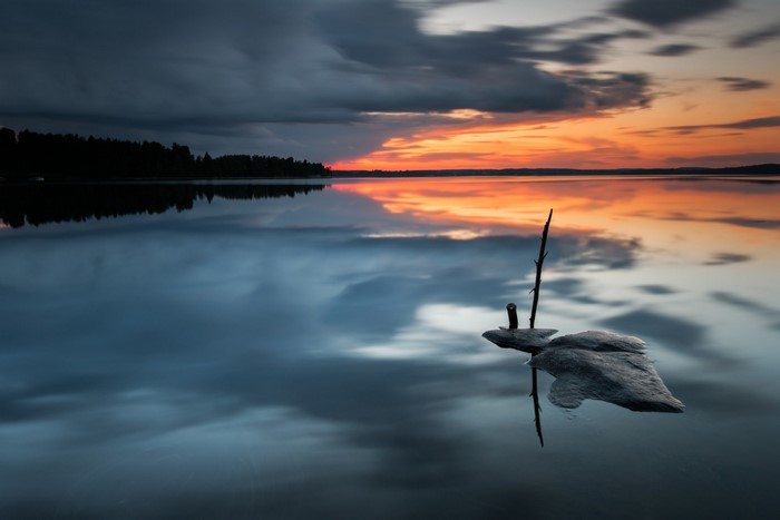 Sunset over a calm lake with a rock and stick