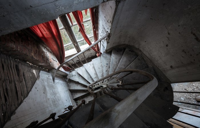 Abandoned spiral staircase with red curtains and broken window