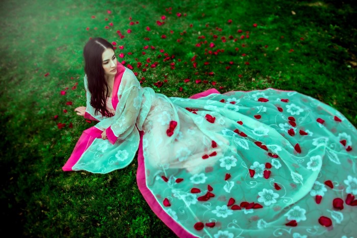 Woman in traditional Asian dress lying on grass with rose petals