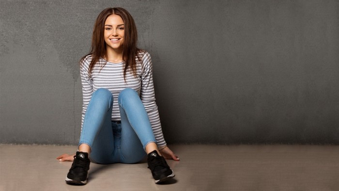 Smiling Woman Sitting Against Gray Wall