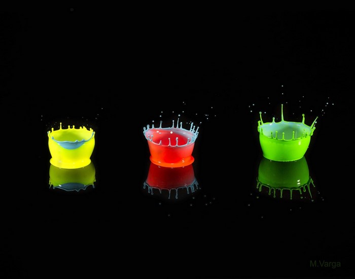 Colorful liquid splashes in cups on black background