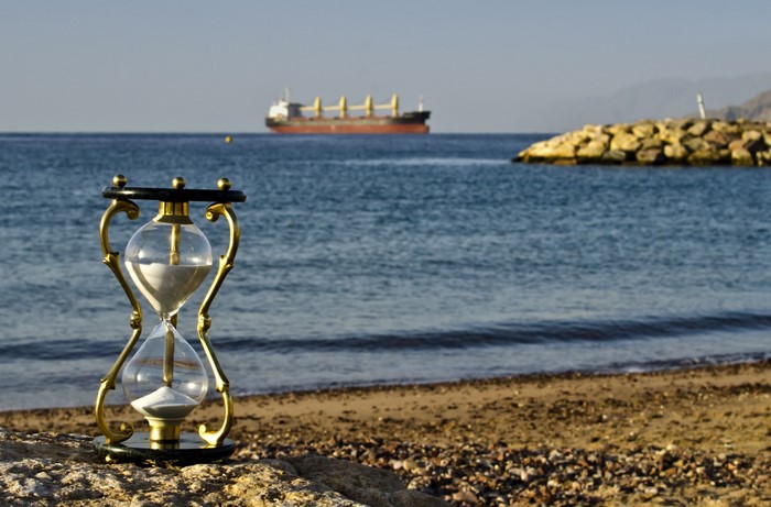Hourglass on a beach with a ship in the sea