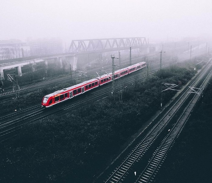 Red train on tracks in fog with bridge