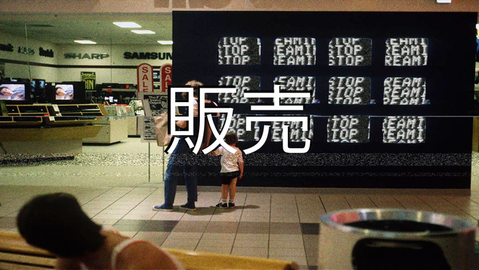 Japanese characters "販売" over a mall electronics store display