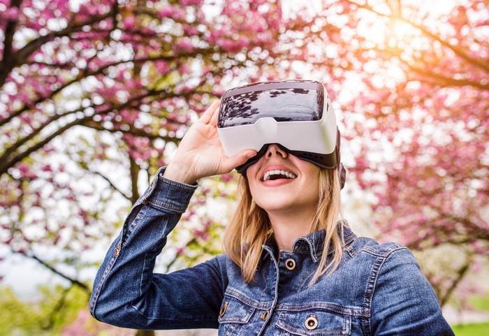 Woman wearing VR headset in a park with blooming trees