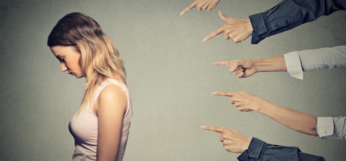 Woman being pointed at by multiple hands
