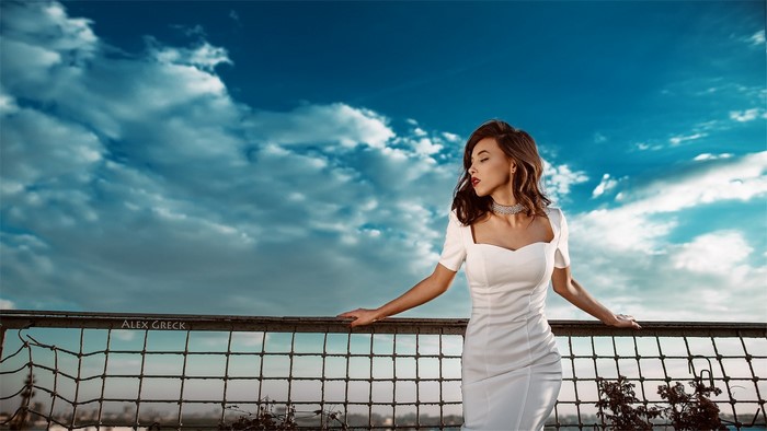 Woman in white dress posing against a cloudy blue sky