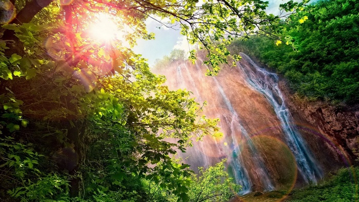 Sunlight streams through trees onto a cascading waterfall