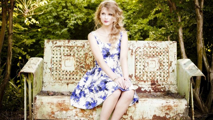 Taylor Swift in a floral dress sitting on a bench