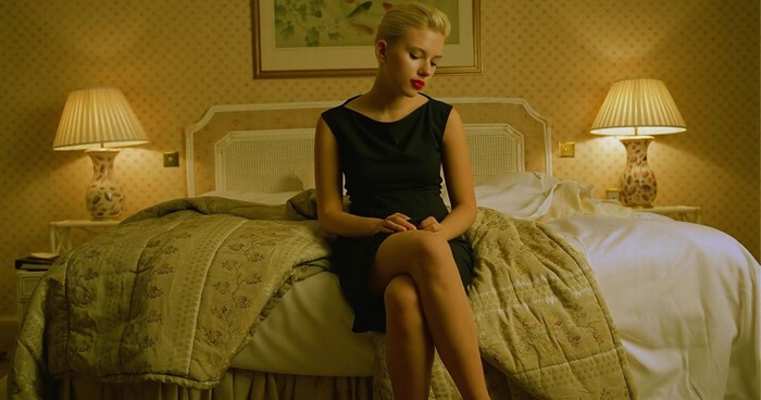 Scarlett Johansson in a black dress sitting on a bed