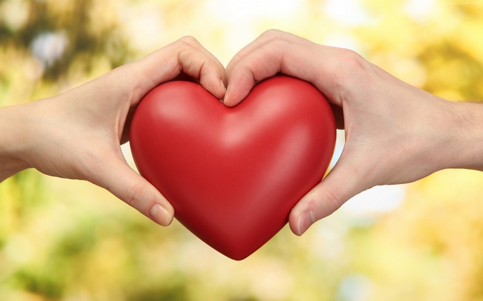 Hands forming a heart shape around a red heart