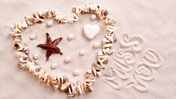 Heart made of shells and pearls on sand with "Miss You" written
