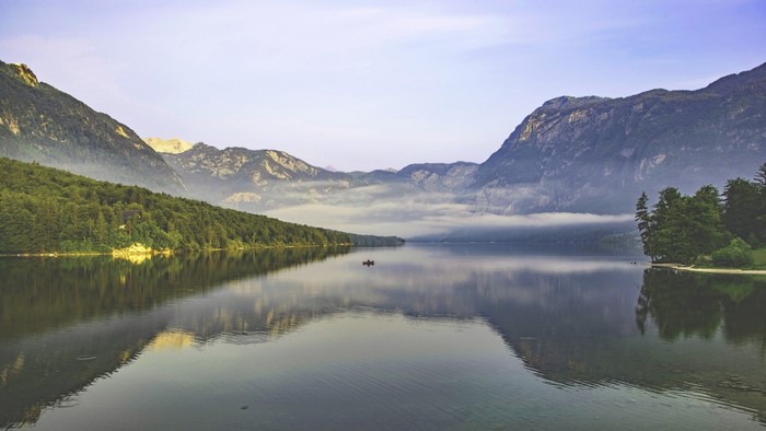 A boat on a misty lake with mountains reflected