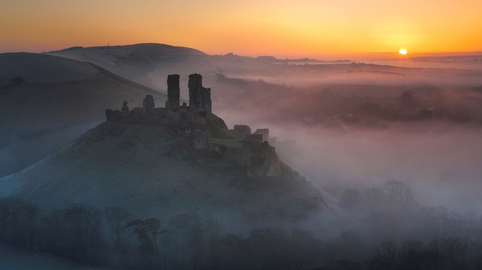 Castle ruins on a hill at sunrise with fog